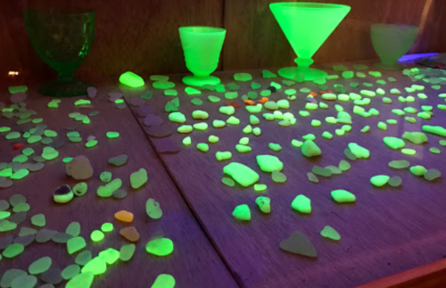 A collection of glowing, colorful glass pieces and stones displayed on a wooden surface under UV light.