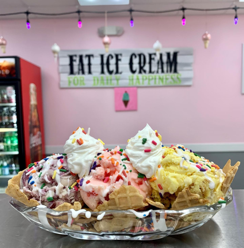 A colorful ice cream sundae in a waffle bowl, topped with whipped cream and sprinkles, in a cheerful ice cream shop.