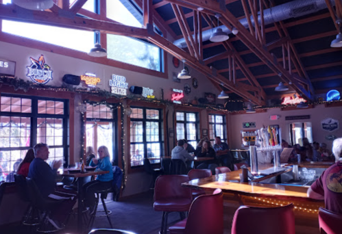 Interior of a lively bar with wooden beams, patrons at tables, and illuminated beer signs on the walls.