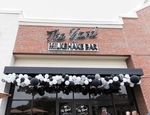 Exterior of The Yard Milkshake Bar, featuring a sign and a decorative balloon arch in black and white.