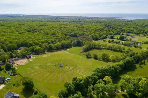 Aerial view of a lush green landscape with a circular pattern in the center, surrounded by trees and fields.