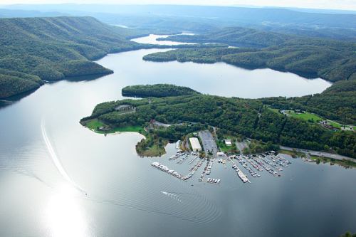 Aerial view of a serene lake surrounded by lush green hills and a marina with boats.