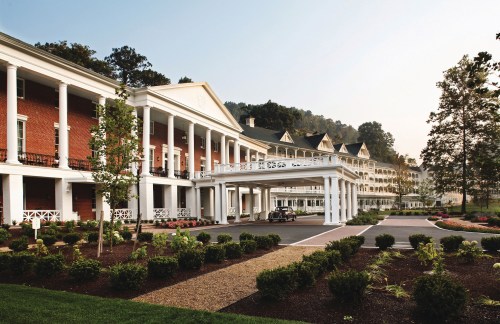 A grand hotel with white columns and brick facade, surrounded by landscaped gardens and trees.