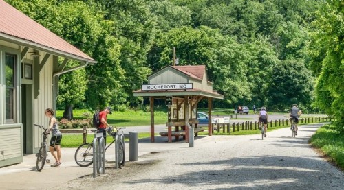 A scenic view of Rocheport, MO, featuring a bike path, a train station, and cyclists enjoying the outdoors.