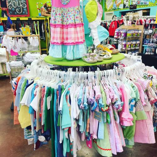 A colorful display of children's clothing in a store, featuring dresses, shirts, and accessories on hangers.