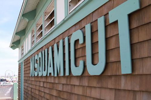 Close-up of the wooden exterior of a building featuring the word "MISQUAMICUT" in large, light blue letters.