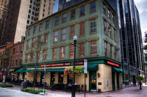 Historic green building with outdoor seating, featuring "Dani Brothers Bar & Grill" signage, surrounded by modern architecture.
