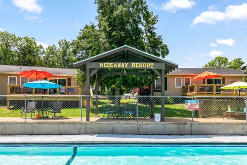 A view of Hideaway Resort with colorful umbrellas, a pool in the foreground, and cozy cabins in the background.
