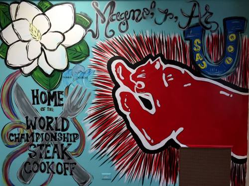 Colorful mural featuring a magnolia flower, steak cook-off text, and a red hand symbol against a blue background.