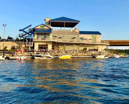 A waterfront building with a blue roof, surrounded by boats docked in calm water under a clear sky.