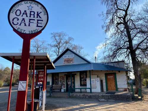Historic general store and café with a sign, surrounded by trees and a dirt road.