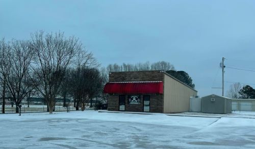 A small brick building with a red awning, surrounded by snow and bare trees under a gray sky.