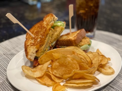 A toasted sandwich with lettuce and a side of crispy potato chips, accompanied by a glass of cola.