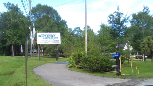 Sign for Bluff Creek Campground with a grassy entrance and trees in the background.