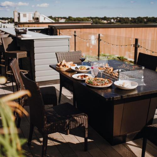 A rooftop dining setup with a table of various dishes and drinks, surrounded by chairs and a scenic view.