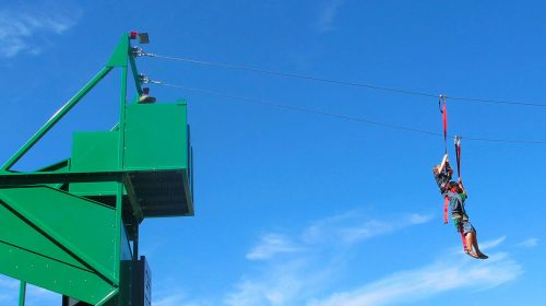 A person zip-lining from a green tower against a clear blue sky.