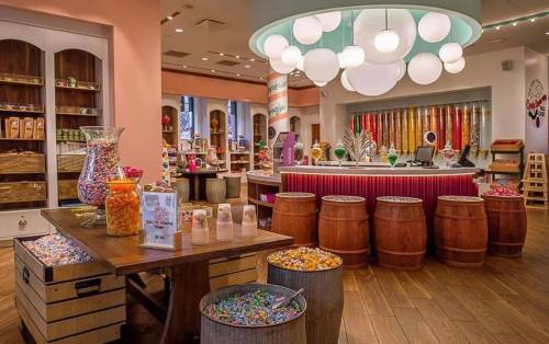 A colorful candy shop interior with jars of sweets, wooden barrels, and a bright chandelier.