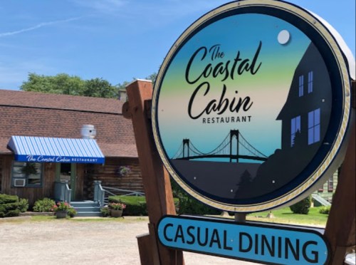 Sign for The Coastal Cabin Restaurant, featuring a bridge and a house silhouette, with a casual dining theme.