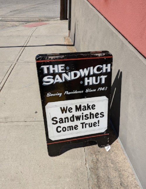 A sidewalk sign for The Sandwich Hut, stating "We Make Sandwiches Come True!" with a vintage design.