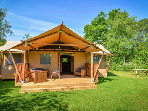A spacious glamping tent with a wooden deck, surrounded by greenery and blue skies.