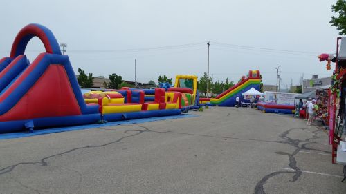 Colorful inflatable bounce houses and slides set up in a parking lot for a community event, with people in the background.
