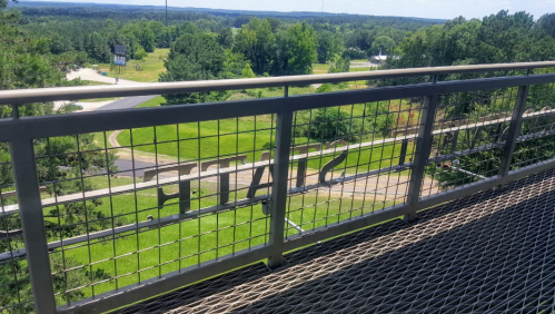 View from a balcony with a metal railing displaying the word "STATE," overlooking a green landscape and road.