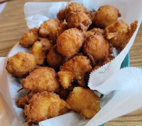 A basket filled with golden-brown, crispy fried corn fritters on a bed of white paper.
