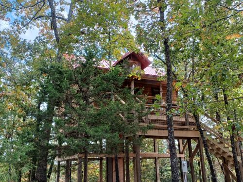 A wooden treehouse nestled among green trees, featuring a red roof and surrounded by autumn foliage.