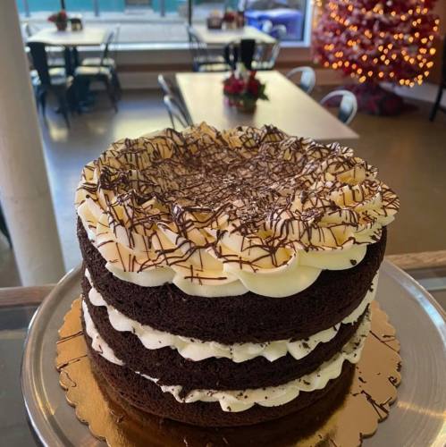 A three-layer chocolate cake with white frosting and chocolate shavings, displayed in a cozy café setting.