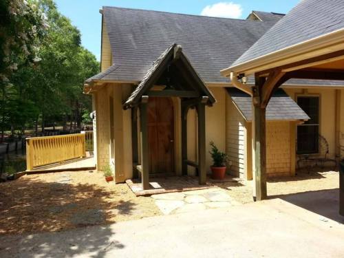 A charming house entrance with a wooden door, surrounded by greenery and a gravel pathway.
