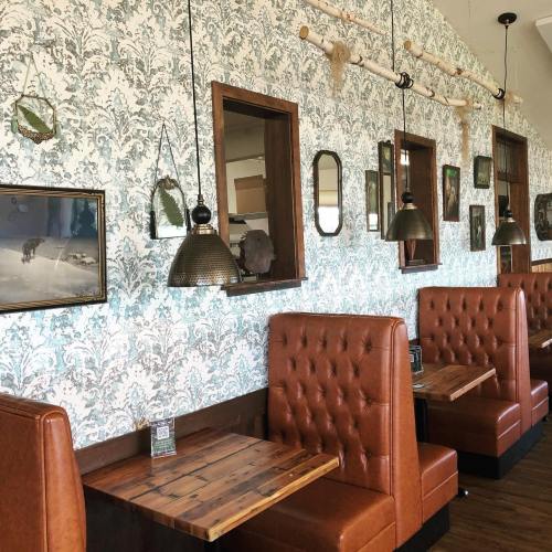 Cozy restaurant interior featuring tufted brown booths, patterned wallpaper, and decorative mirrors.
