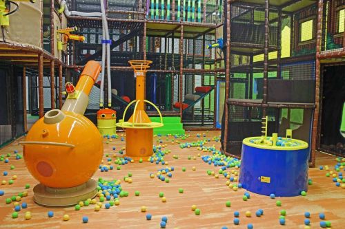 Colorful indoor play area with climbing structures, ball pits, and interactive toys scattered across the floor.