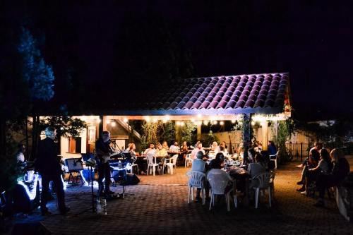 A lively outdoor gathering at night, with guests seated around tables under string lights and a musician performing nearby.
