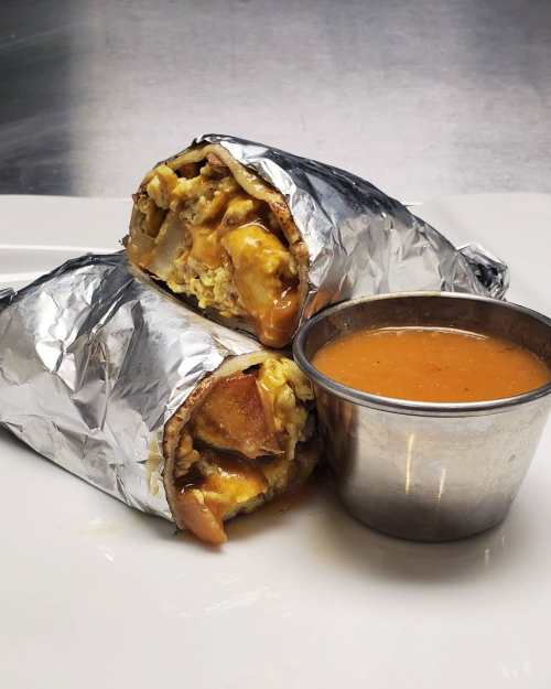 Two foil-wrapped burritos with a side of orange sauce on a white plate.
