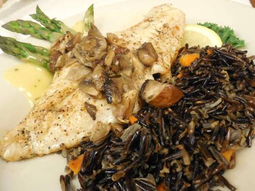 Grilled fish fillet topped with mushrooms, served with wild rice and asparagus on a white plate.