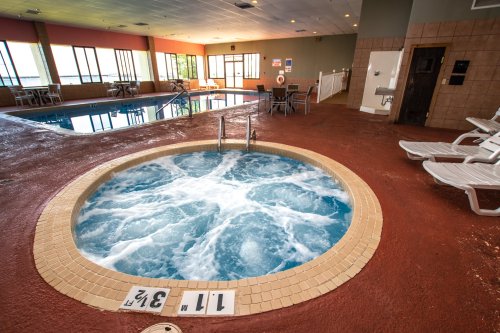 Indoor pool area featuring a hot tub with bubbling water, lounge chairs, and large windows for natural light.