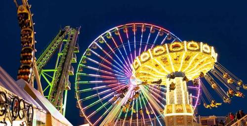 Colorful amusement park rides illuminated at night, featuring a Ferris wheel and a swing ride.