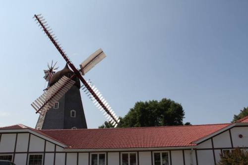 A tall windmill with large blades stands beside a building with a red roof under a clear blue sky.