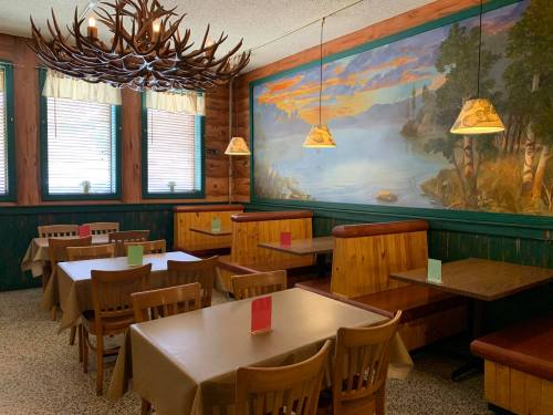 Cozy restaurant interior with wooden booths, tables, and a scenic mural of a lake and mountains on the wall.