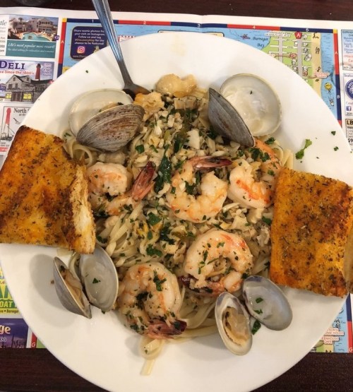 A plate of shrimp and clam pasta with garlic bread, garnished with parsley, on a colorful placemat.