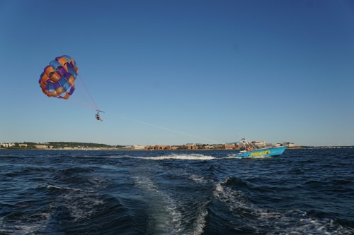 A person parasails above the water, being towed by a colorful boat on a clear, sunny day.