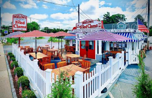 Outdoor seating area of a seafood restaurant with striped umbrellas, white fences, and signs for fried clams.