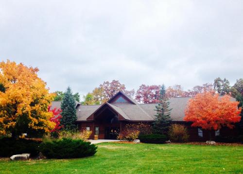 A cozy wooden house surrounded by vibrant autumn trees in shades of orange and red under a cloudy sky.