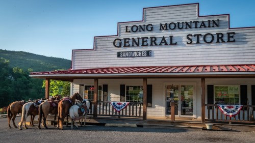Horses tied up outside the Long Mountain General Store, featuring a red roof and patriotic decorations.