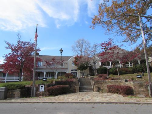 A building with a flagpole and landscaped steps, surrounded by trees with autumn foliage.