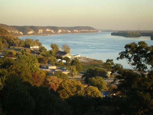 A scenic view of a river winding through lush greenery and hills, with a small town visible along the shore.