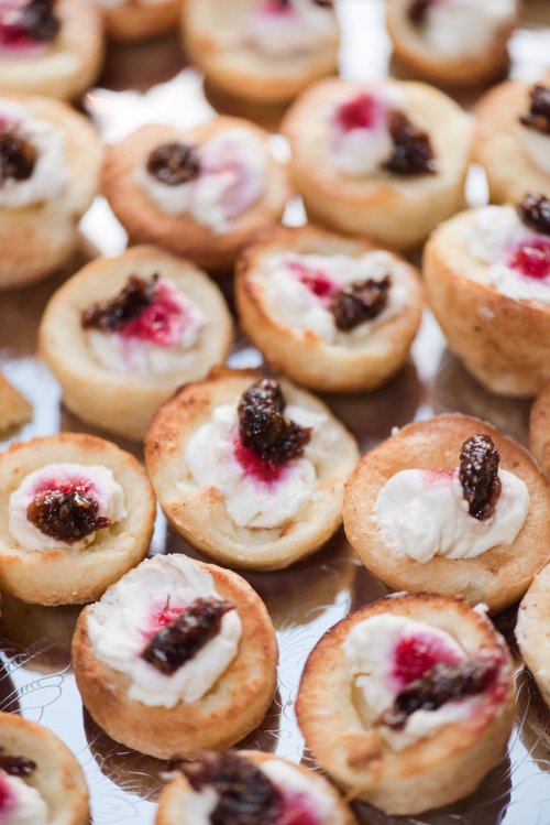 A close-up of mini pastry cups filled with cream and topped with a dark fruit preserve.