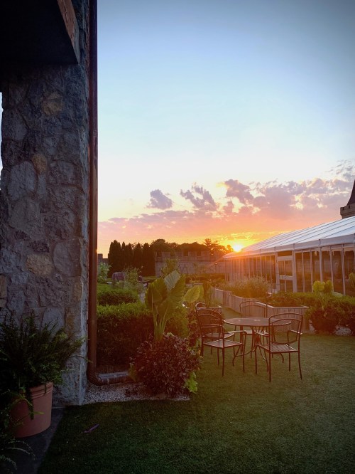 Sunset view from a rooftop garden, featuring plants, chairs, and a glass-enclosed area against a colorful sky.