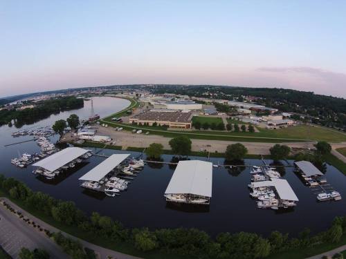 Aerial view of a marina with boats docked, surrounded by trees and a river, with a town in the background.