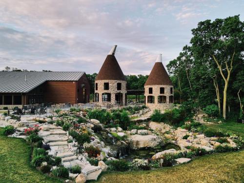 Two unique stone buildings with conical roofs surrounded by a landscaped garden and a small pond.